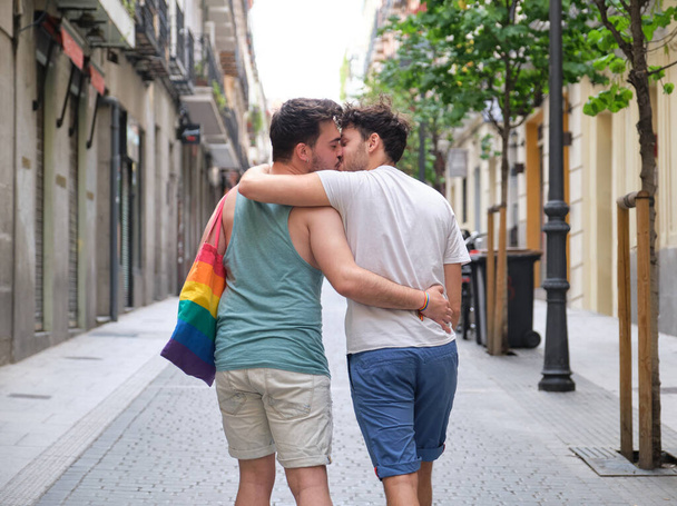 Homopari nauraa ja halailee penkillä pitäen LGBT-lippuja. - Valokuva, kuva