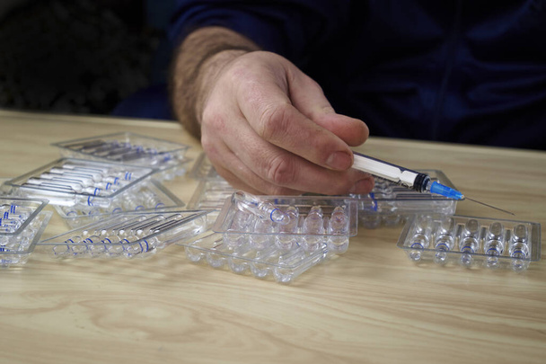 Mann legt Ampullen mit Medikamenten auf den Tisch und eine Spritze in die Hand - Foto, Bild