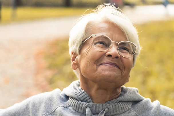 Ritratto ravvicinato di una vecchia nonna in pensione che sorride e trascorre il suo tempo libero all'aperto, godendo del bel tempo e dell'aria fresca. - Foto, immagini