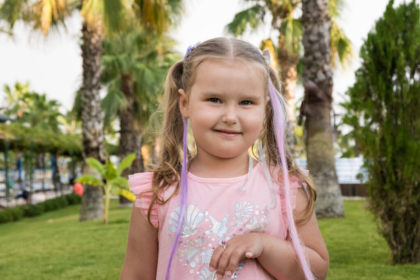 Portret van een schattig meisje 4 jaar oud gekleed in een multi gekleurde jurk tegen de achtergrond van palmbomen - Foto, afbeelding