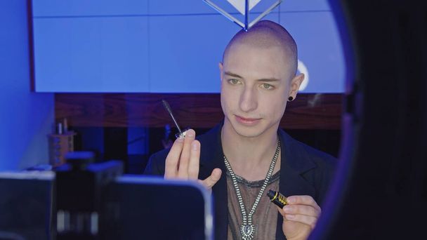 niet-binaire Europese persoon leert hoe om hun make-up te doen en zet mascara op wimpers van video tutorials in de badkamer  - Foto, afbeelding