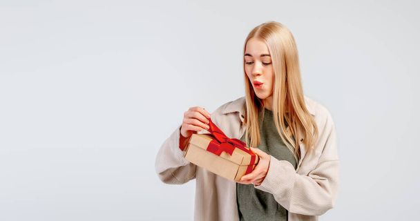 Excited young woman opening present gift box. Pretty girl smiling and posing with gift box on light background. New Year Women's Day birthday holiday concept. Copy space for your text - Photo, Image