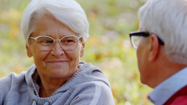 Ältere grauhaarige Großeltern lächeln einander an und unterhalten sich, während sie Zeit im Freien verbringen. - Foto, Bild