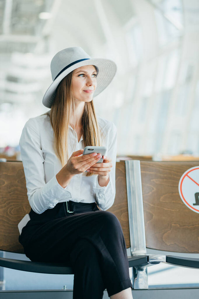 Woman Reading Phone Messages in Airport Waiting Room. Happy girl buying e-ticket, making hotel reservations and checking in online - Photo, image