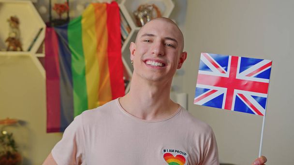 Vnitřní portrét hrdého bělocha, usmívajícího se gaye, mávajícího ve svém bytě vlajkou UKs. - Fotografie, Obrázek
