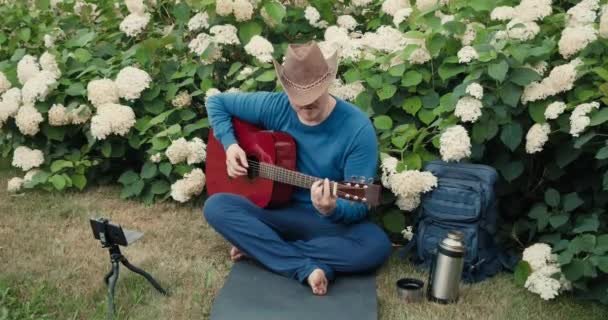 Mies matkustava kitara, istuu puistossa luonnossa ja tekee online-lähetys - Materiaali, video