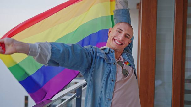 queer Ευρωπαίος μέλος της κοινότητας Igbt χορεύει με υπερηφάνεια gay σημαία σε ένα μπαλκόνι - Φωτογραφία, εικόνα