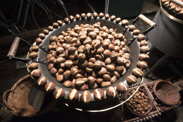 a chestnut vendor roasting chestnuts, delicious edible nuts with brown shell - Photo, Image