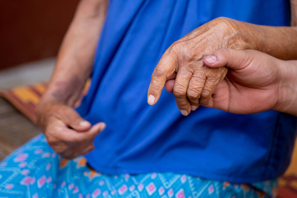 Detailní záběr na ruce staré dámy Muž držící babiččinu ruku vypadá, že se vřele stará o starší v rodině Stará dáma s tradičními thajskými šaty - Fotografie, Obrázek