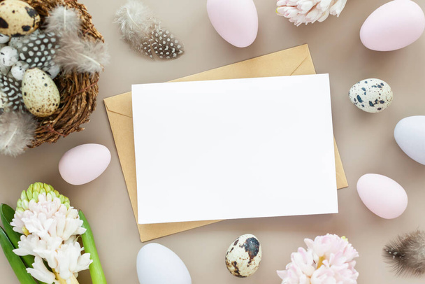 Easter mockup with blank letter, easter eggs and flowers on a neutral background. Flat lay greeting card with space for text. Easter decoration, Easter design template. - Foto, imagen