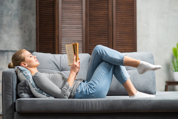 Young blonde girl is reading a book or a textbook. A beautiful woman is resting and relaxing at home. - Foto, afbeelding
