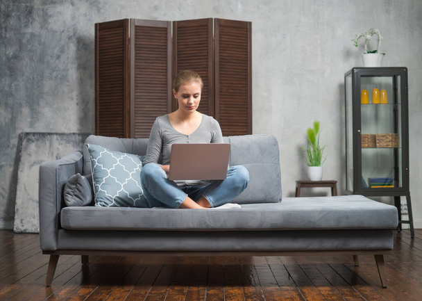 Young woman works using a laptop lying on the couch. Student, entrepreneur or freelancer girl working or studying remotely via internet. - Photo, image