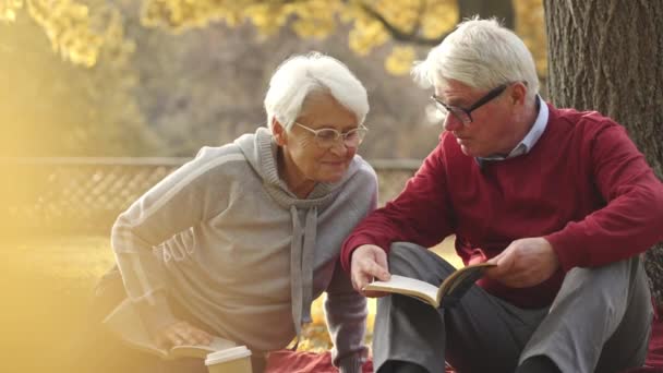 Sposato anziani caucasici seduti su un terreno, facendo un picnic, e leggendo un romanzo. - Filmati, video