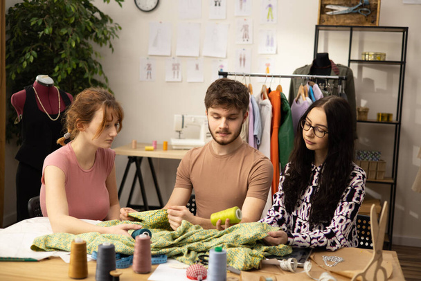 The work of fashion designer and tailors in the shop. Fashion designers working in their studio. Colorful Fabrics, Clothes Hanging and Sewing Items are Visible. - Photo, Image