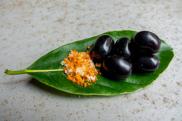 Würzig gemischtes Salz mit einigen schwarzen Java-Pflaumenfrüchten in den grünen Blättern. Eine Möglichkeit, reife Cäsium-Camini-Früchte von Hand zu essen. 4k Nahaufnahme-Video. - Foto, Bild