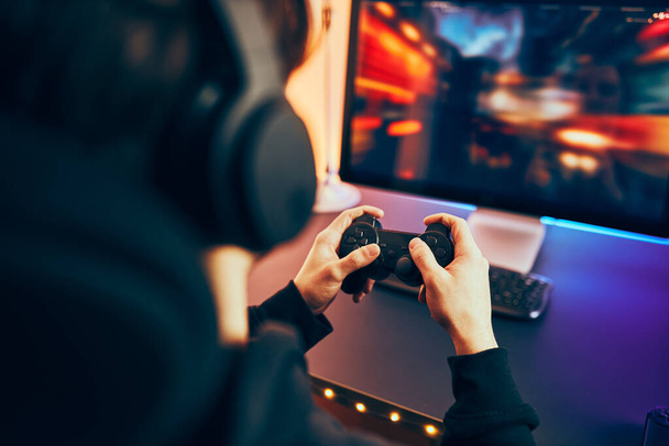 Man playing video game at home. Gamer holding gamepads sitting at front of screen. Streamer playing online in dark room lit by neon lights. Competition and having fun - Foto, Bild