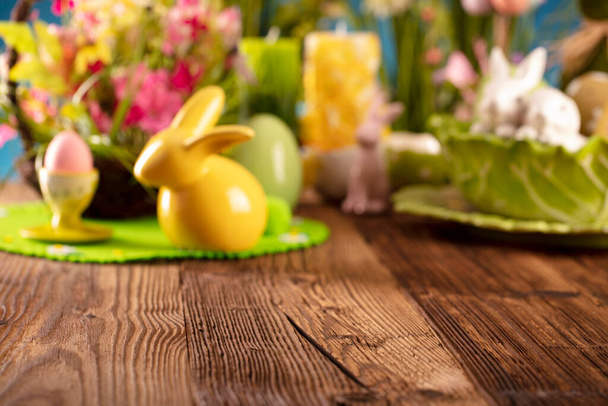 Easter time. Easter decorations on the rustic wooden table. Easter bunny, easter eggs in basket and cabbage leaf. Bouquets of spring flowers.  - Фото, изображение