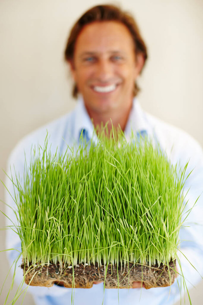 Everything fresh and green. Shot of a man holding out a patch of grass. - Photo, Image