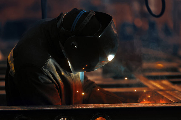 Welder at work. Welding of metal sparks and smoke in the workshop. Industrial Welder With gas Torch in Protective Helmet, welding metal profiles. The welding operation at construction site - Zdjęcie, obraz