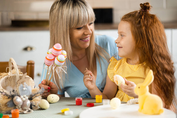 Happy mother and her beloved daughter paint Easter eggs - Foto, afbeelding