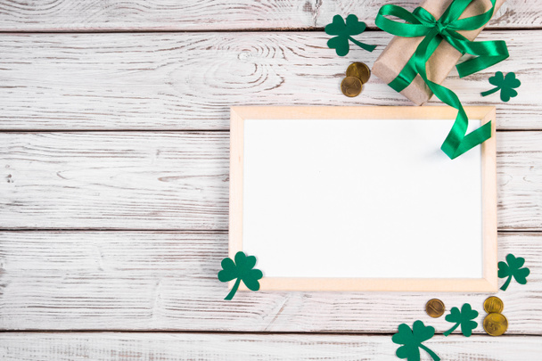 Gelukkig St. Patricks Day concept. Klaver shamrock, gouden munten en een geschenk met een groen lint op een witte achtergrond. Feestelijke samenstelling. - Foto, afbeelding