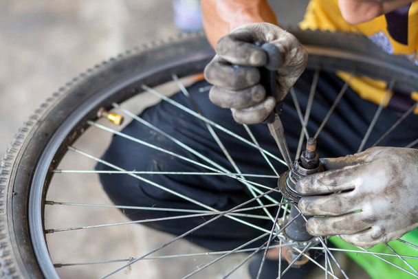 Close-up De as van het fietswiel wordt met beschermende handschoenen geboord door de handen van een ervaren beoefenaar. Olievlekken die de wiellagers versterken. Thaise monteur - Foto, afbeelding