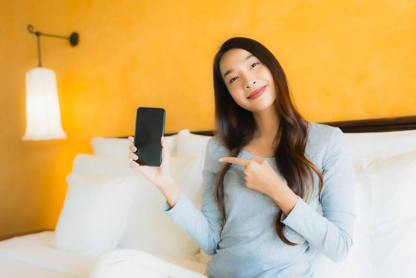Portrait beautiful young asian woman using mobile cell phone on bed with coffee cup in bedroom interior - 写真・画像