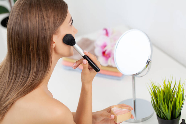 Μελαχρινή όμορφη γυναίκα κάνει μακιγιάζ μπροστά από τον καθρέφτη - Φωτογραφία, εικόνα
