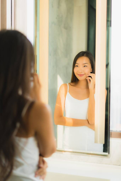 Retrato hermosa joven asiática mujer comprobar su cara y facial en baño interior - Foto, Imagen