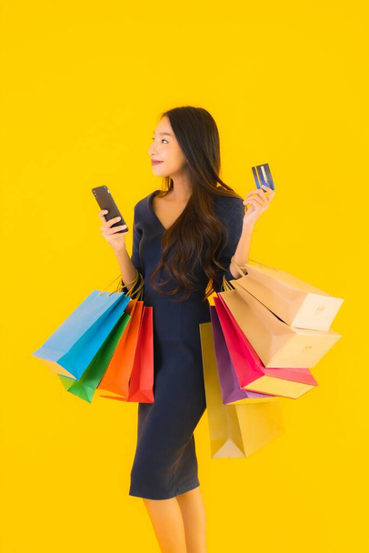 Retrato hermosa joven asiática mujer con bolsa de compras tarjeta de crédito y teléfono móvil inteligente amarillo aislado fondo
 - Foto, Imagen
