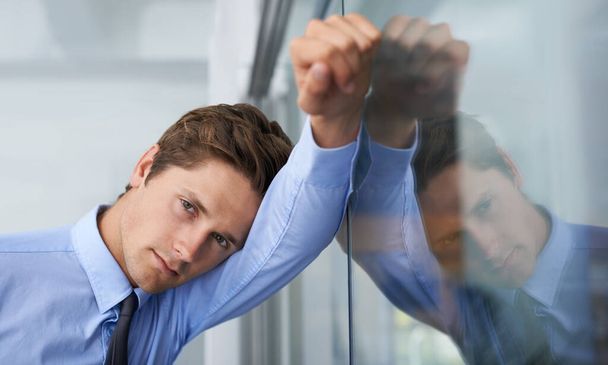 Hes feeling the pressure. A tired young businessman leaning against a glass wall. - Fotoğraf, Görsel