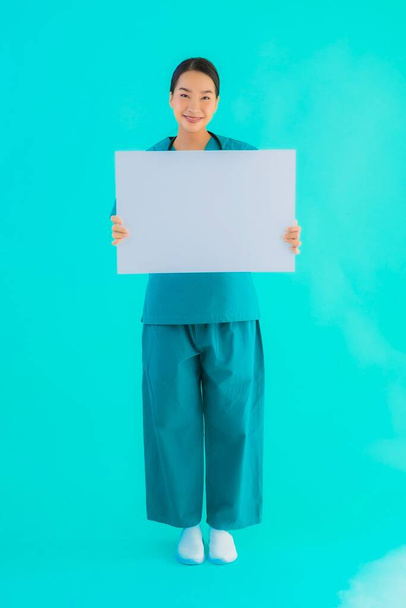 Retrato hermosa joven asiática médico mujer con tablero de papel vacío para el espacio de copia sobre fondo azul aislado - Salud en el hospital y el concepto de clínica
 - Foto, Imagen