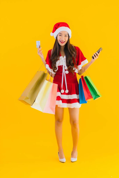 Portrait beautiful young asian woman wear christmas clothes hat with a lot of shopping bag on yellow isolated background - Zdjęcie, obraz