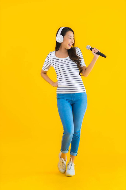 Portrait beautiful young asian woman singing with microphone and headphone on yellow isolated background - Foto, Imagem