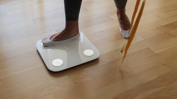 Женщина наступает на весы для измерения массы тела в домашних условиях.  - Фото, изображение