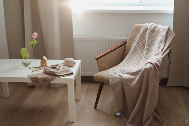 cozy home interior decor with a chair, plaid, table and knitting needles with threads, beige yarn.  - Foto, Bild
