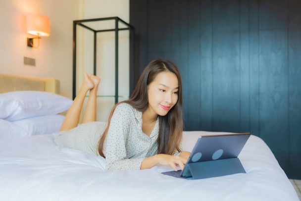 Retrato hermosa joven mujer asiática uso tableta con tarjeta de crédito en la cama en el interior del dormitorio - Foto, imagen