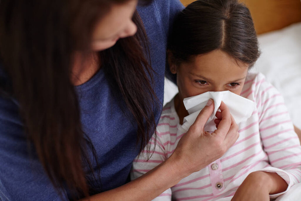 When a cold strikes.... Shot of a mother helping her sick daughter to blow her nose. - Foto, Imagen