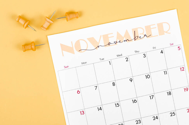 The November 2022 calendar and wooden push pin on yellow background. - Foto, imagen
