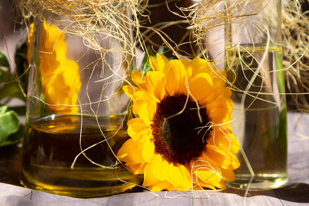 Butelki szklane z olejem wewnątrz i słonecznika kwiaty ozdobione raffia. - Zdjęcie, obraz