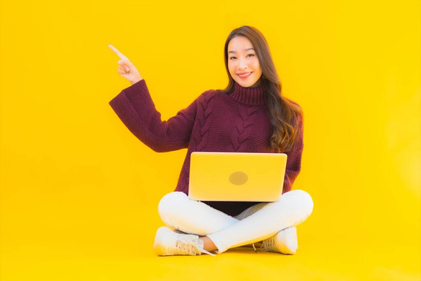 Портрет красивая молодая азиатская женщина использовать компьютер ноутбук на желтом фоне изолированы - Фото, изображение
