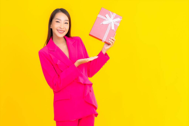 Портрет красива молода азіатка з червоною подарунковою коробкою на жовтому кольорі ізольована на фоні
 - Фото, зображення