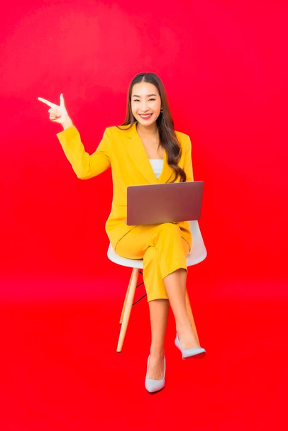 ポートレート美しい若いビジネスアジアの女性は赤の背景にコンピュータのラップトップを使用します - 写真・画像