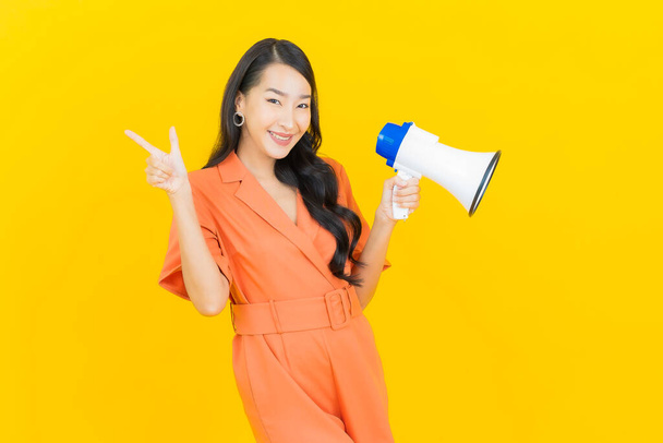 Портрет красива молода азіатка посміхається з мегафоном на жовтому тлі
 - Фото, зображення