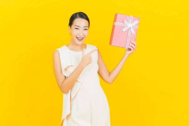 Asyalı güzel bir kadının portresi. Sarı arka planda kırmızı hediye kutusuyla gülümsüyor. - Fotoğraf, Görsel