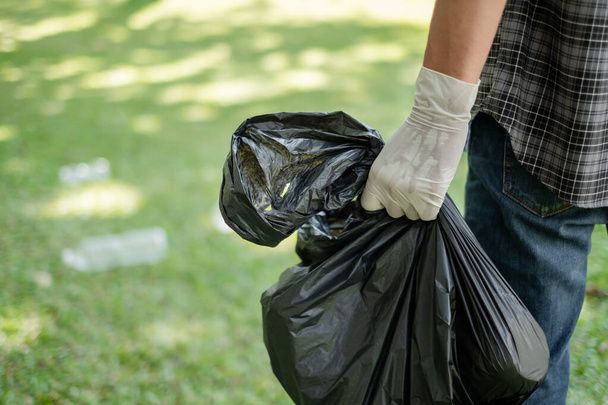 raccolta dei rifiuti, le mani dell'uomo raccolgono bottiglie di plastica, mettono spazzatura in sacchi neri per pulire nei parchi, evitare l'inquinamento, essere amichevole per l'ambiente e l'ecosistema. - Foto, immagini