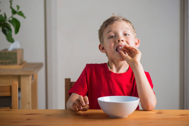 Милый мальчик ест мюсли на завтрак. Портрет в стиле жизни.  - Фото, изображение