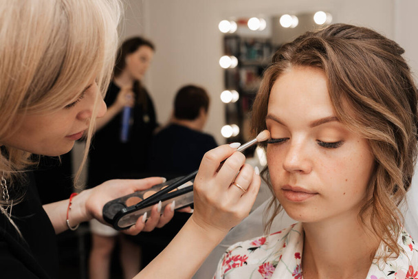 Shooting in a beauty salon. makeup artist applies makeup to the bride - Fotó, kép
