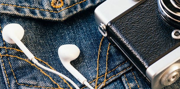 Film camera and white wired headphones lie against background of denim. Fashionable hipster background. Retro style. - Photo, Image