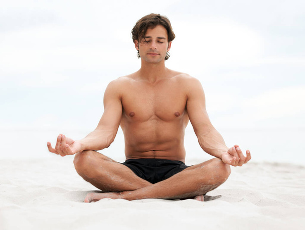 Sakin ol ve doğanın söyleyeceklerini dinle. Genç yakışıklı adam sahilde oturmuş meditasyon yapıyor.. - Fotoğraf, Görsel